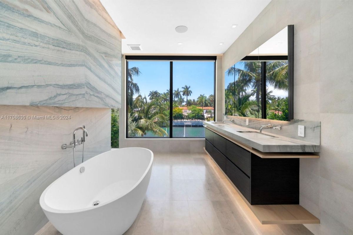 Luxurious bathroom featuring a freestanding soaking tub, double vanity with a marble countertop, and large windows showcasing lush tropical views.