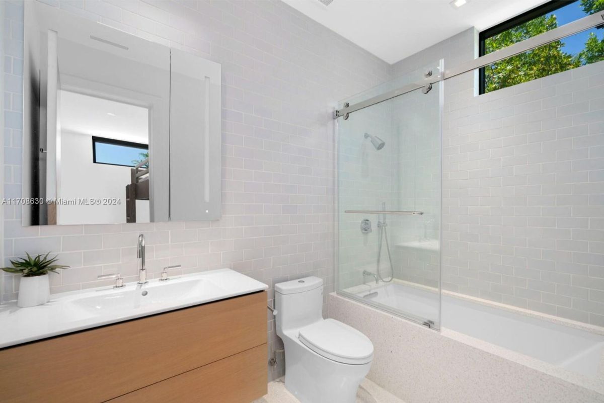 Bright bathroom with a sleek vanity, subway tile walls, and a glass-enclosed bathtub.