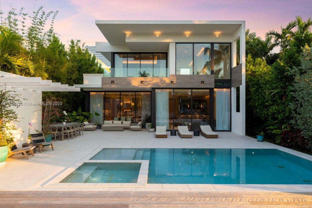 Two-story modern home with expansive glass walls overlooking a pristine pool and lush greenery.