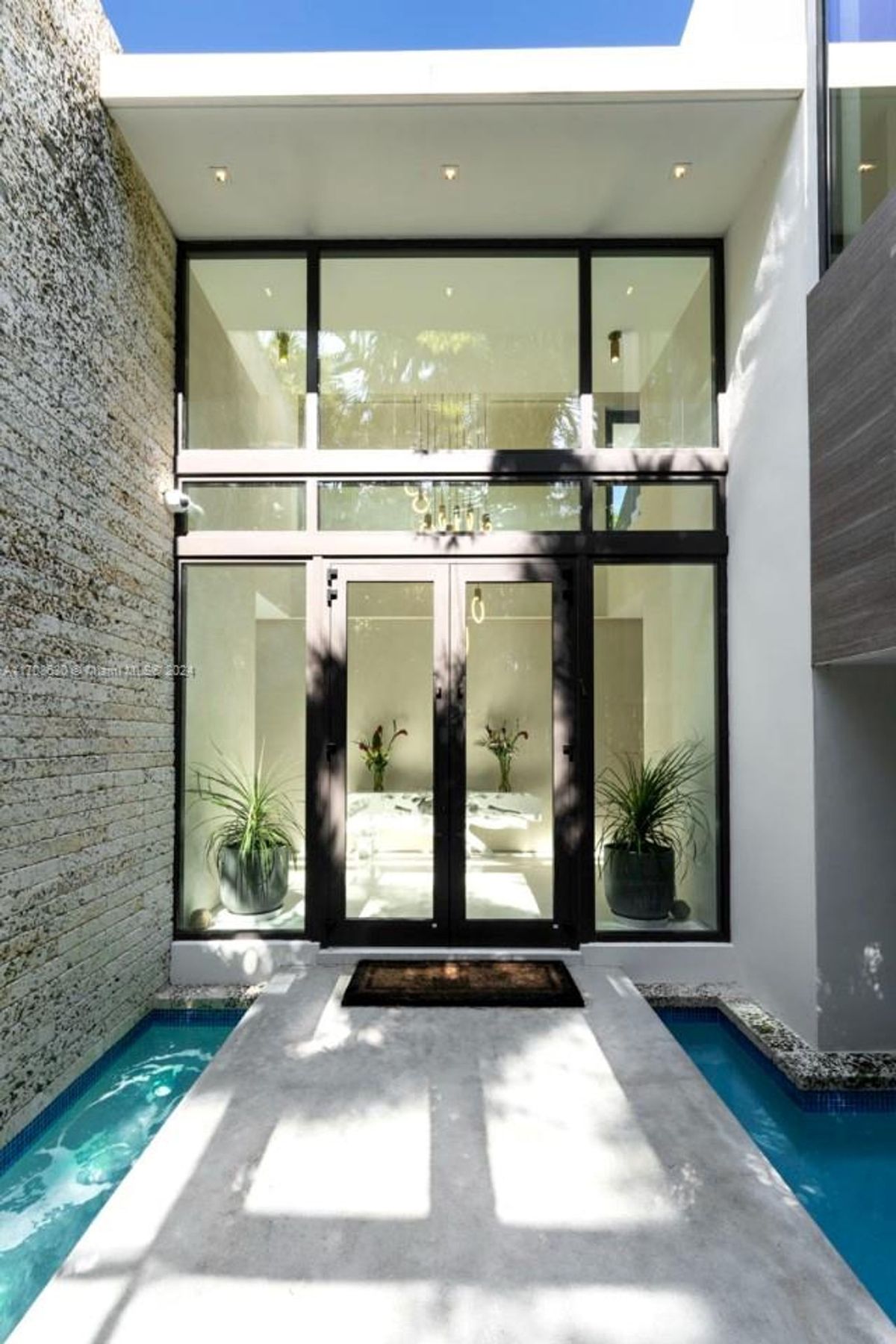 Modern double-door entry framed by tall windows and accented with a tranquil water feature.