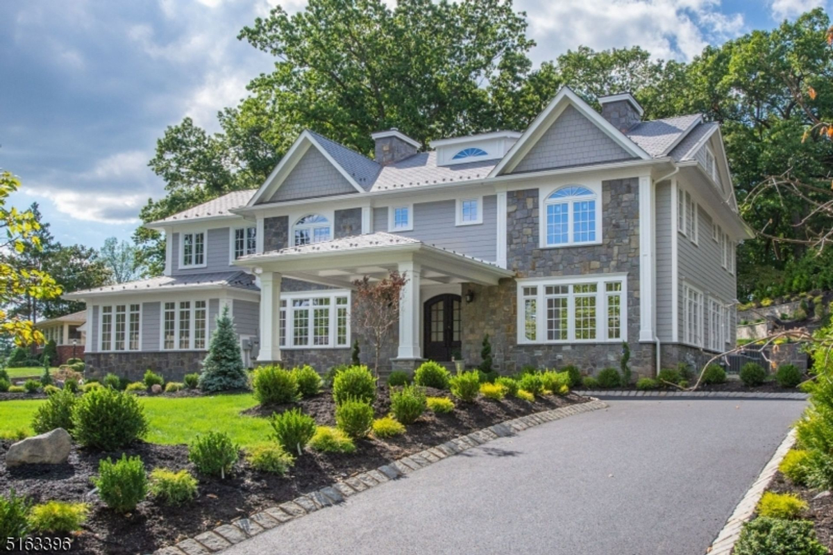 A stately, stone-accented colonial home framed by lush greenery and a manicured driveway.