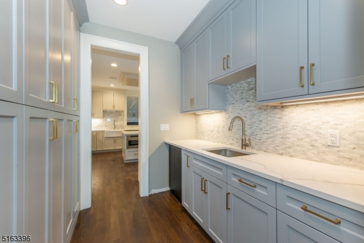 Chic butler's pantry features custom gray cabinetry, brass hardware, marble backsplash, and built-in under-cabinet lighting.