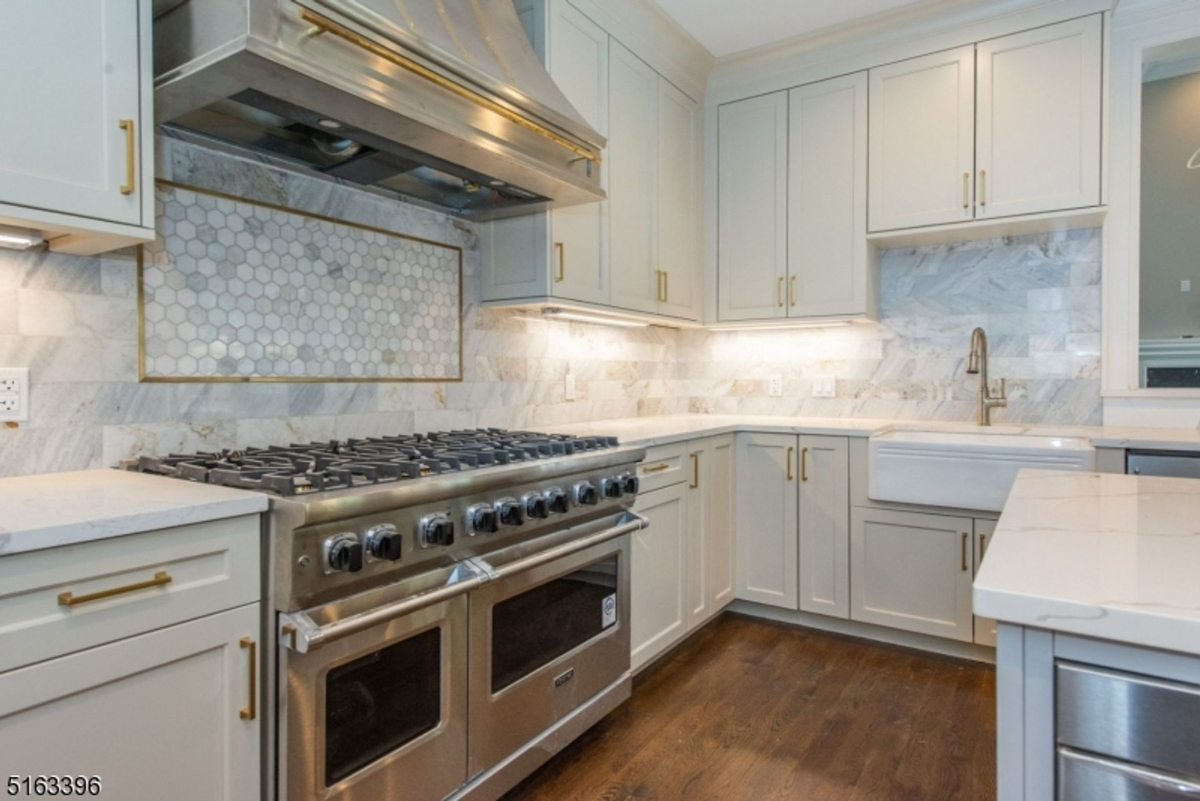 Professional-grade kitchen showcases a six-burner gas range with double ovens, custom marble backsplash with gold accents, and a farmhouse sink.