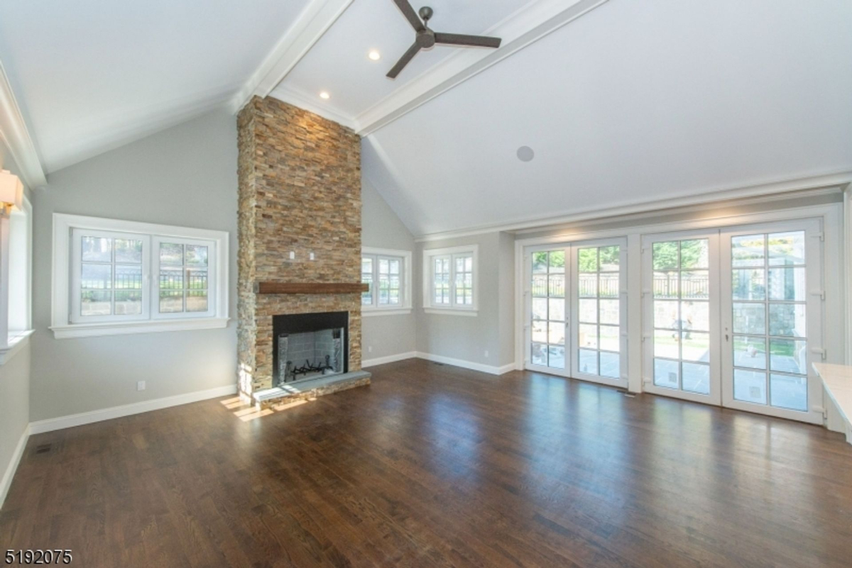 Vaulted ceiling enhances the spacious living room featuring a stone fireplace and abundant natural light through French doors.