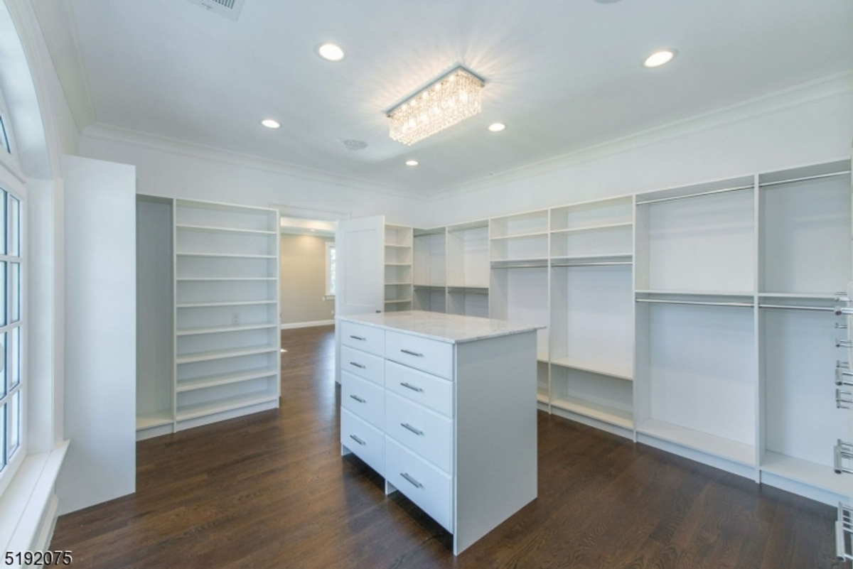 Expansive walk-in closet features custom shelving, an island with drawers, and elegant lighting.