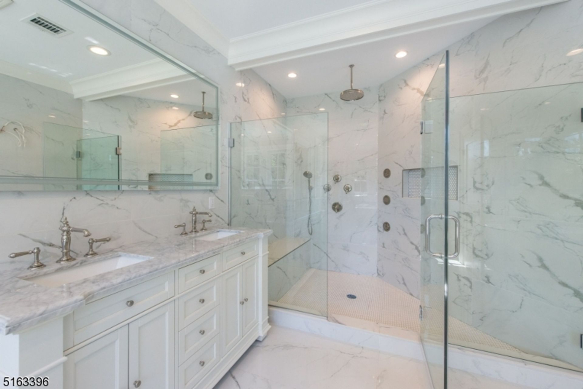 Spa-like shower offers dual rainfall fixtures, body jets, and glass enclosure surrounded by polished marble surfaces.