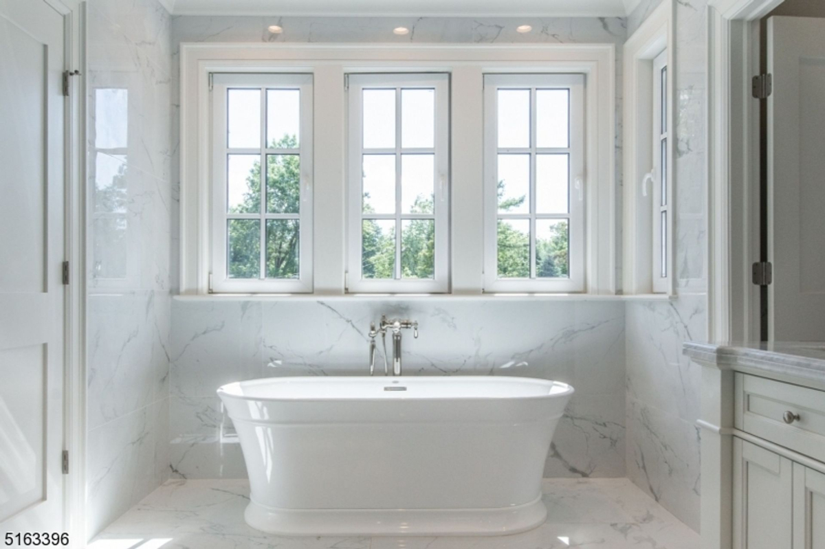 Freestanding tub framed by large windows in a marble bathroom.