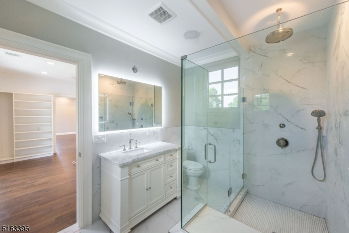 Glass-enclosed shower with marble walls and a sleek vanity.