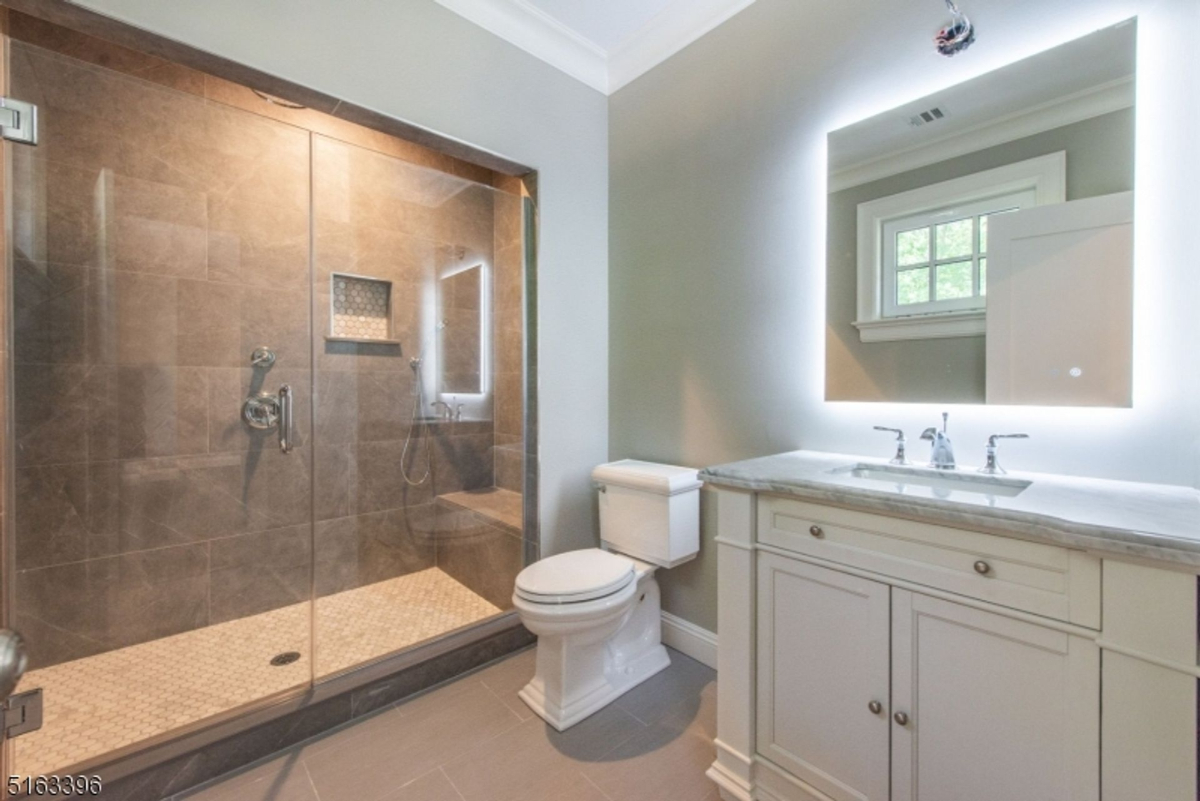 Spacious bathroom featuring a glass shower with built-in niche and illuminated mirror.