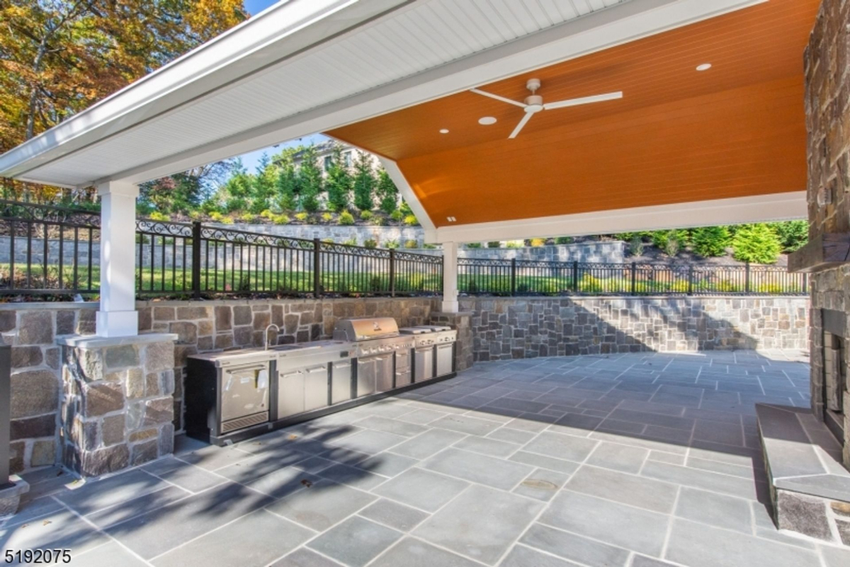 Covered outdoor kitchen with stainless steel appliances and stone finishes.