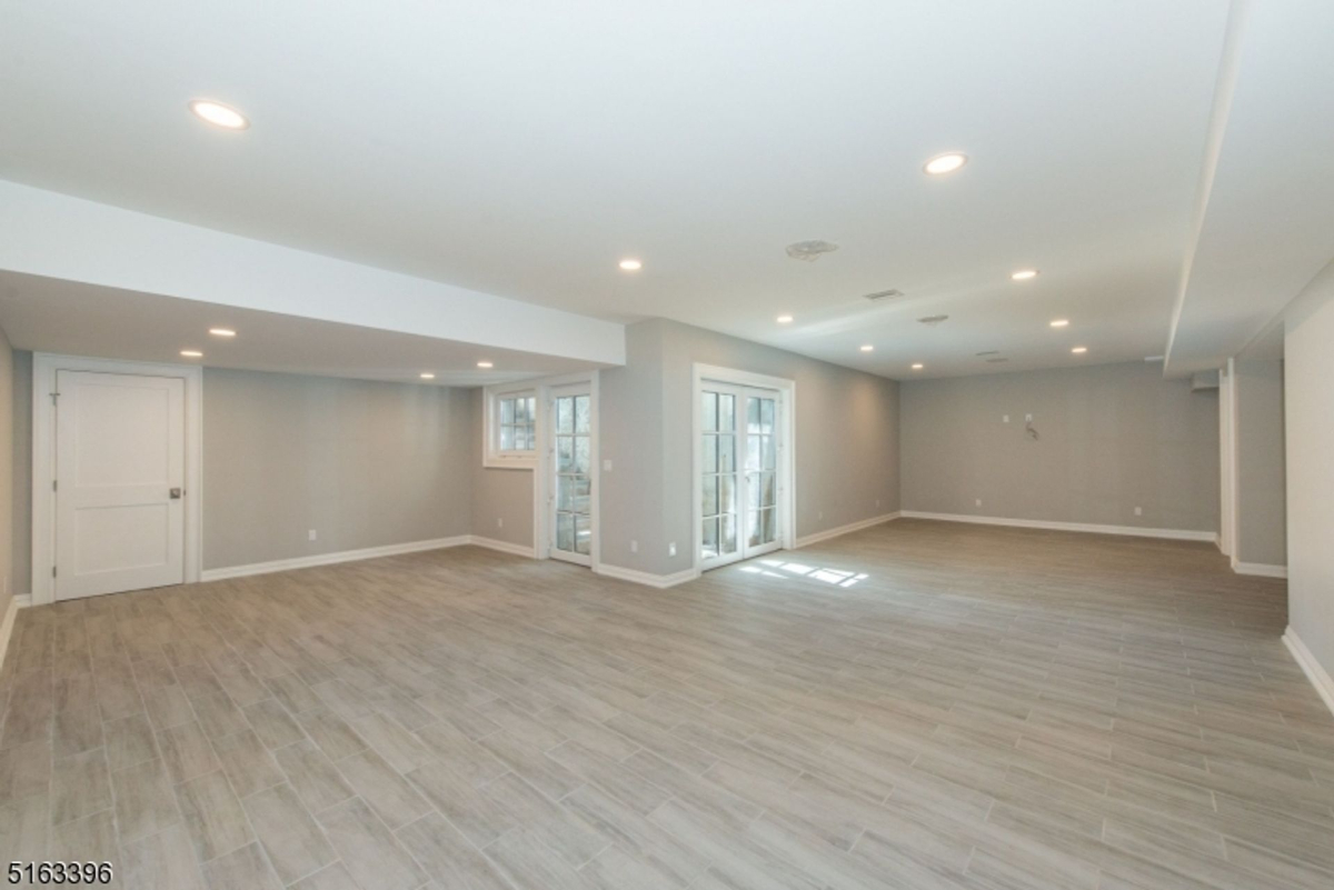 Spacious open-concept basement with modern tile flooring, recessed lighting, and access to the outdoors through French doors.