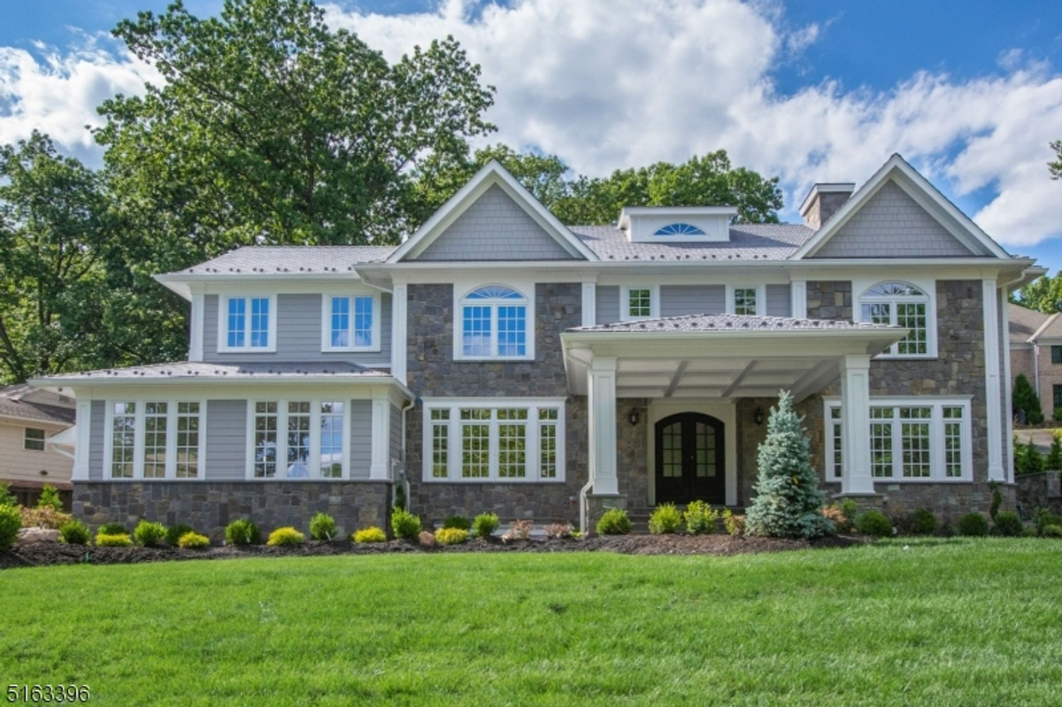 An elegant colonial-style home featuring stone accents, large windows, and a covered front porch.