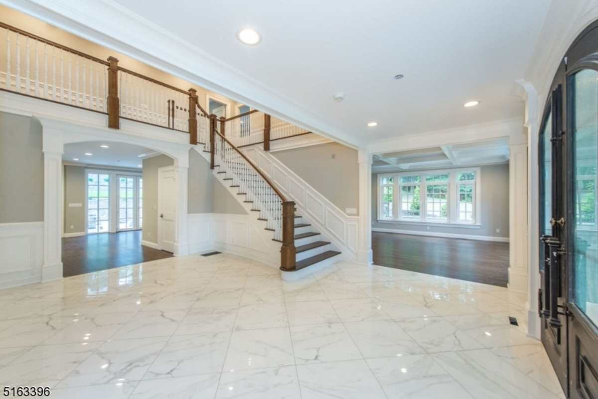 A grand foyer with marble floors, a sweeping staircase, and elegant wood accents.