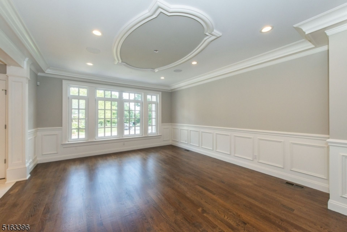 Spacious formal room featuring intricate wainscoting, a sculpted ceiling design, and expansive windows.