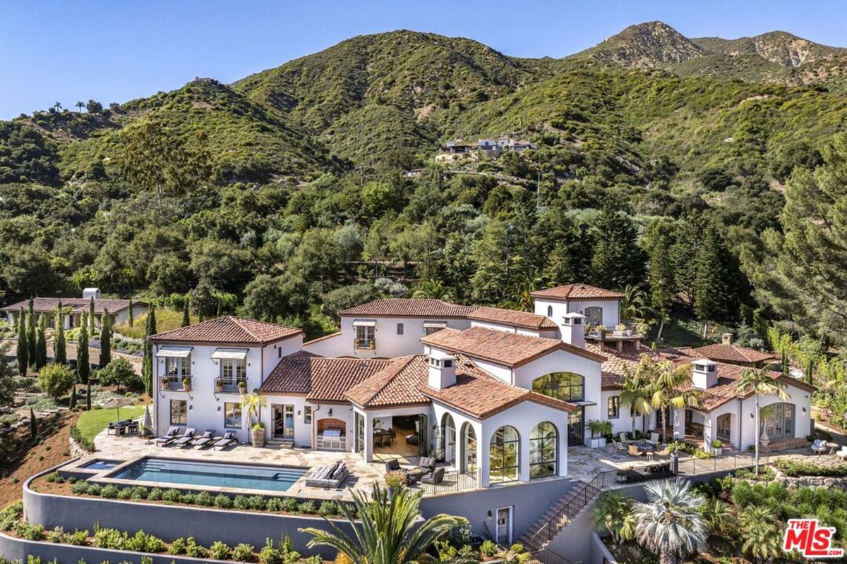 A luxurious Mediterranean-style villa rests elegantly amidst verdant hills, offering breathtaking views and an expansive outdoor pool.