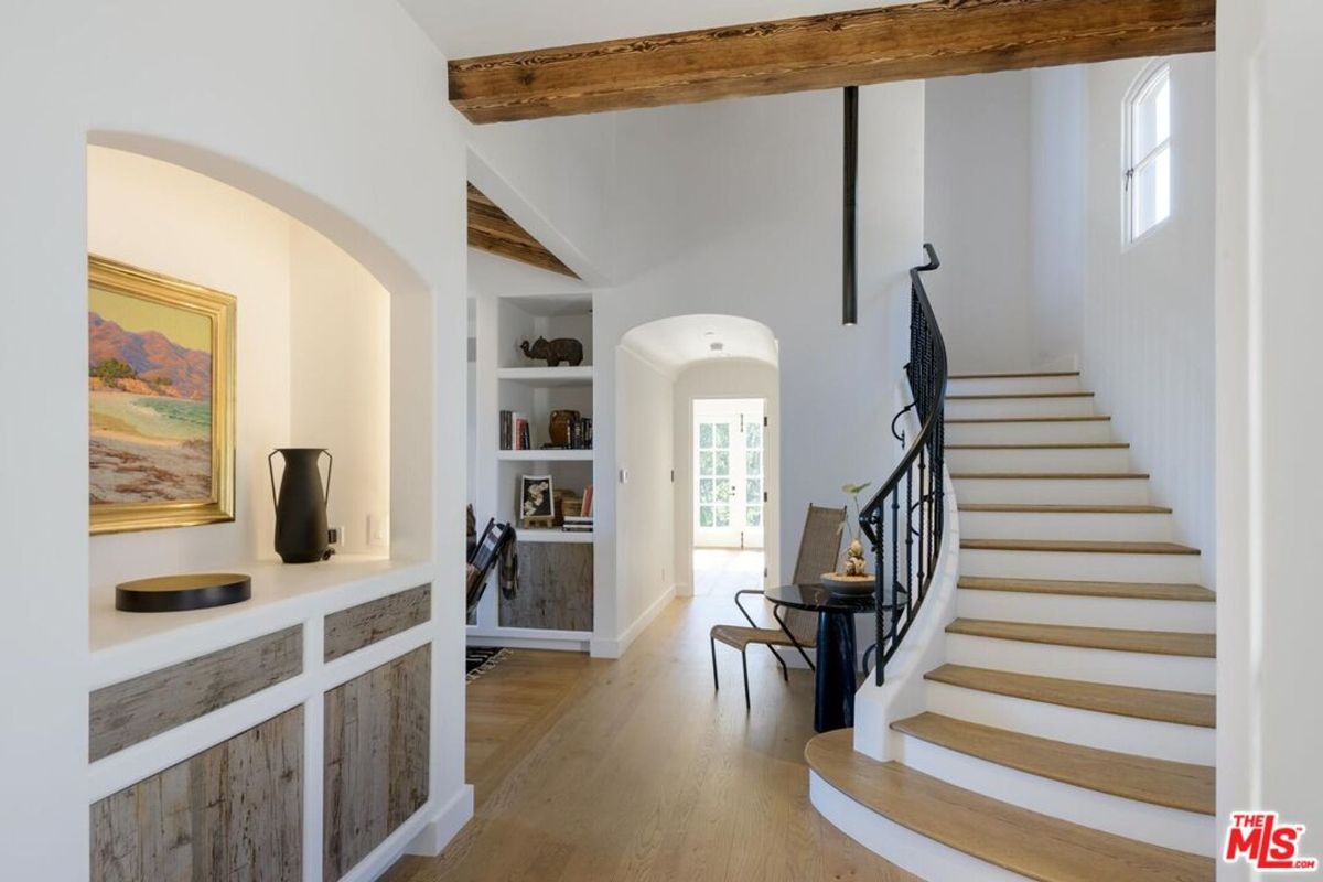 A curved staircase with elegant wrought iron railing enhances this entryway, which features rustic wood panel accents and a cozy reading nook.