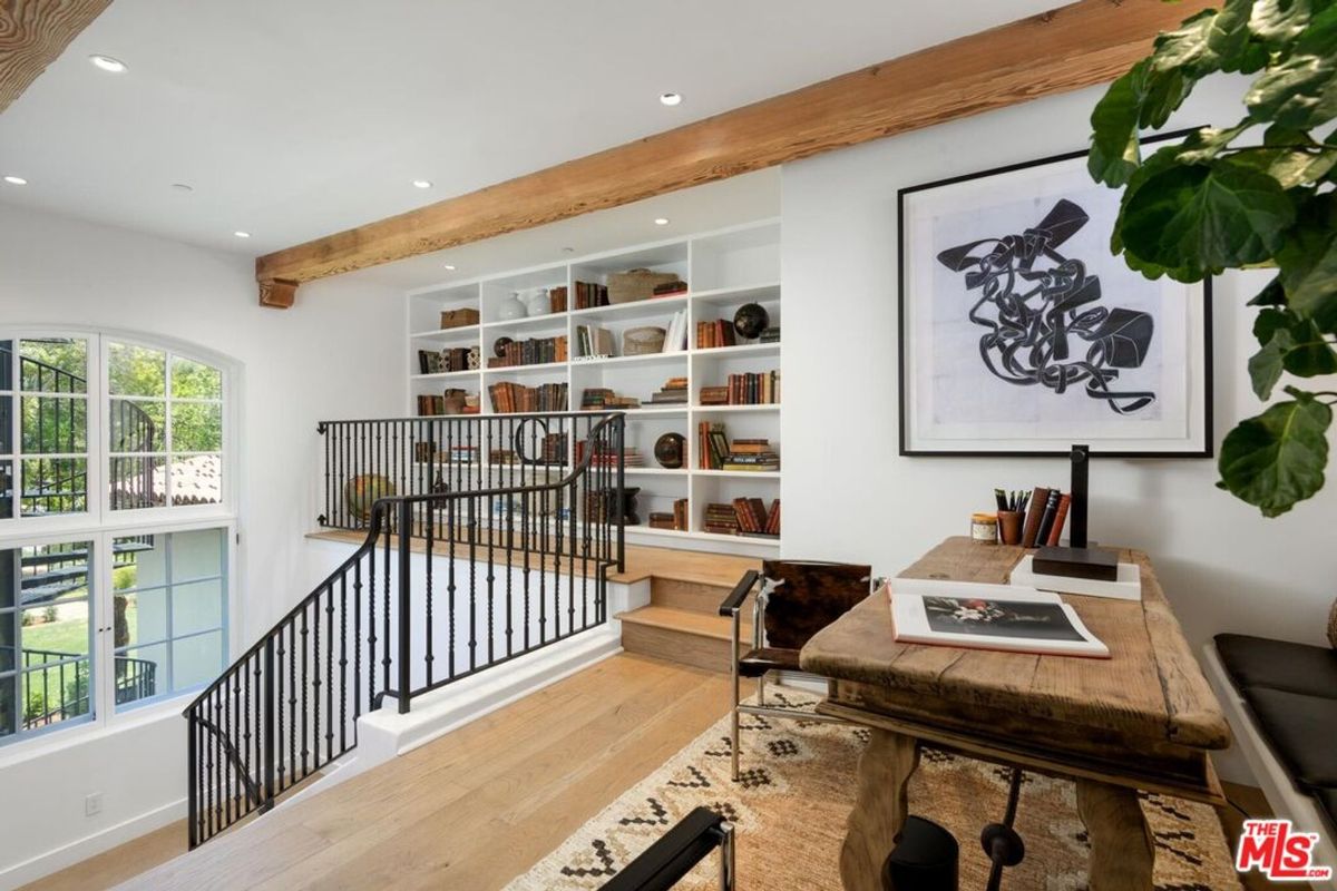 Loft-style library and workspace is enhanced by custom built-in shelves, exposed wooden beams, and a rustic desk, blending charm and practicality.