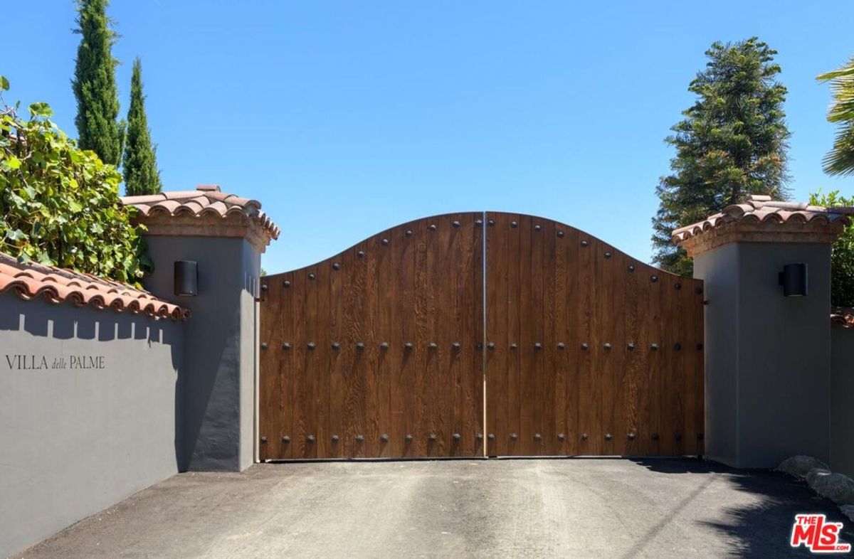 An elegant wooden gate with Mediterranean-style stone pillars marks the entrance to "Villa delle Palme."