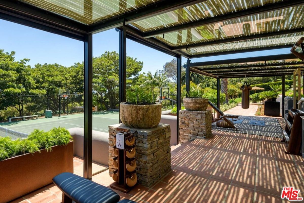 A shaded outdoor gym area overlooks the tennis court, blending fitness with natural surroundings.