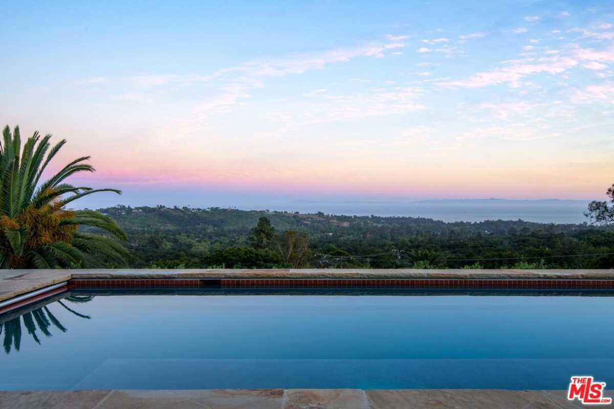 A tranquil infinity pool overlooks sweeping vistas of lush greenery and an enchanting pastel sunset.