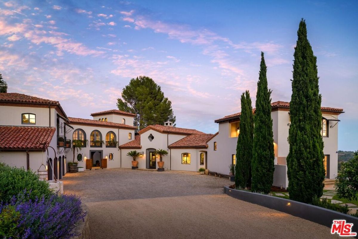 Villa with terracotta rooftops and arched windows is framed by tall cypress trees and a lavender-lined driveway.