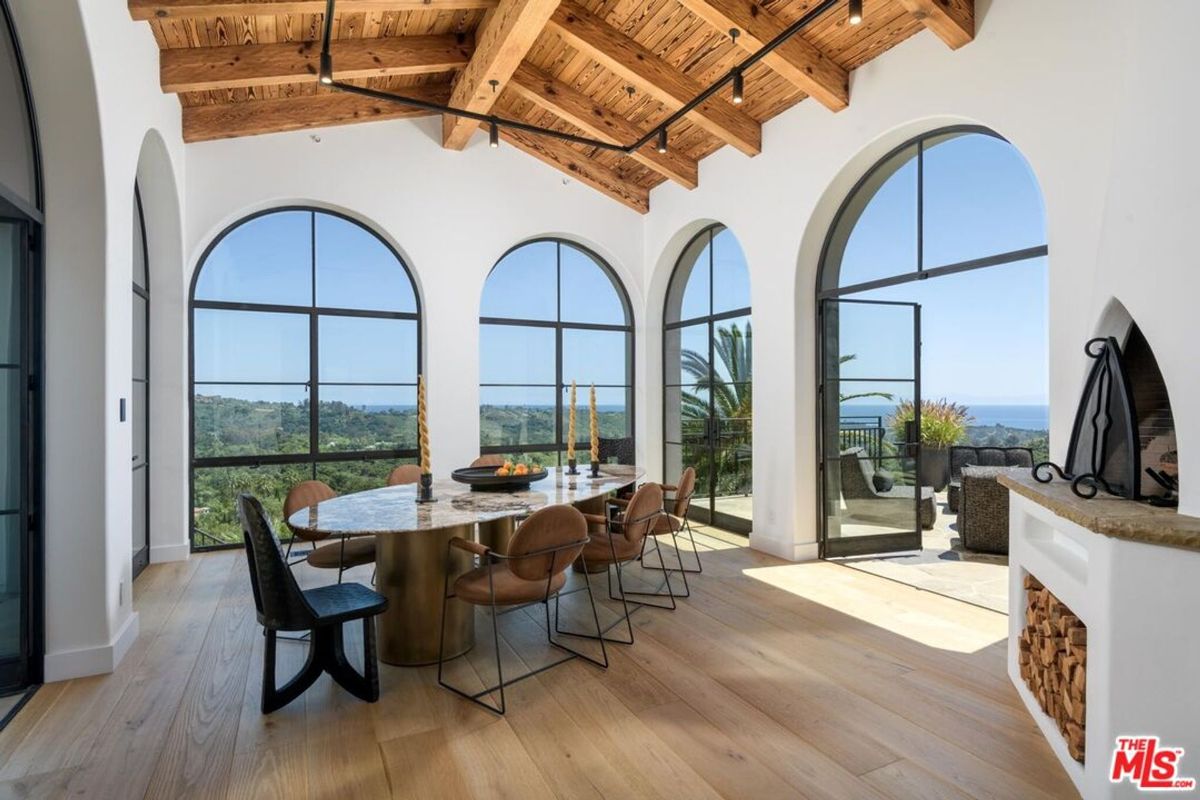 Expansive arched windows frame breathtaking ocean and hillside views in this bright dining room.