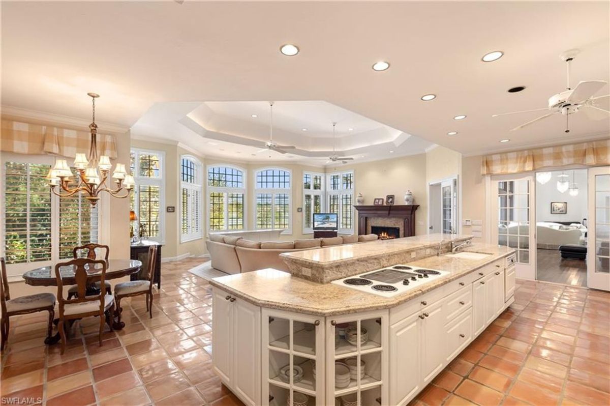 Open-concept kitchen and living area features a spacious island with granite countertops, terracotta flooring, and large arched windows allowing abundant natural light.