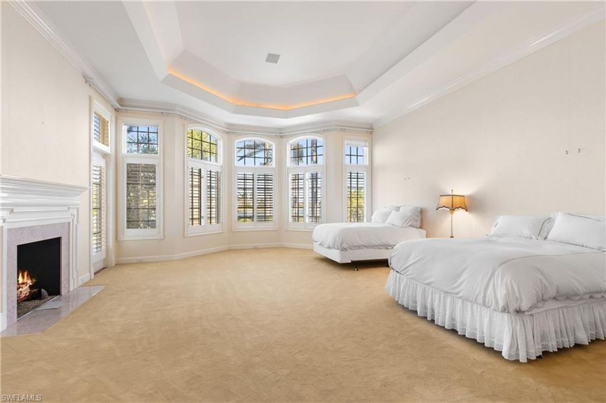 Bedroom exudes elegance with a tray ceiling, large bay windows, a cozy fireplace, and plush carpeting for ultimate comfort.