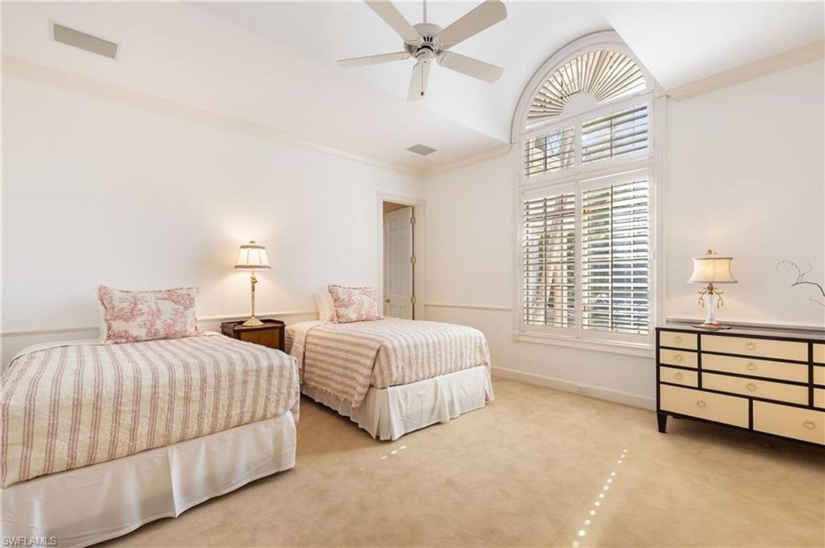 Guest bedroom features twin beds, a vaulted ceiling with an arched window, and plantation shutters for natural light and privacy.