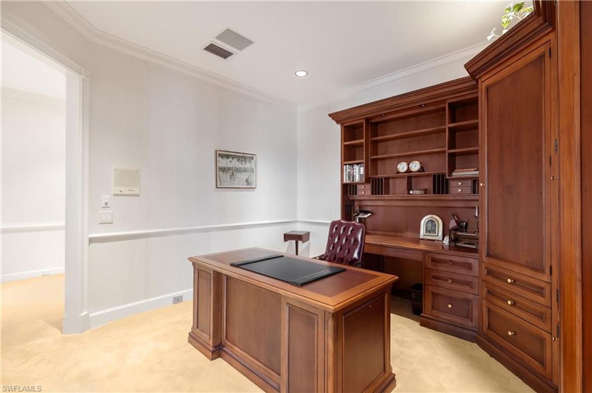 Home office showcases rich wood cabinetry, a classic executive desk, and ample built-in storage for a productive workspace.