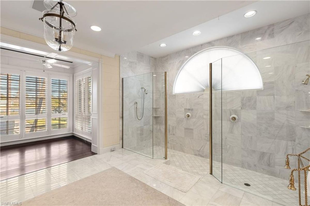 Luxurious spa-like bathroom features dual glass-enclosed rain showers, marble tiles, and a semi-arched frosted window for natural light and privacy.