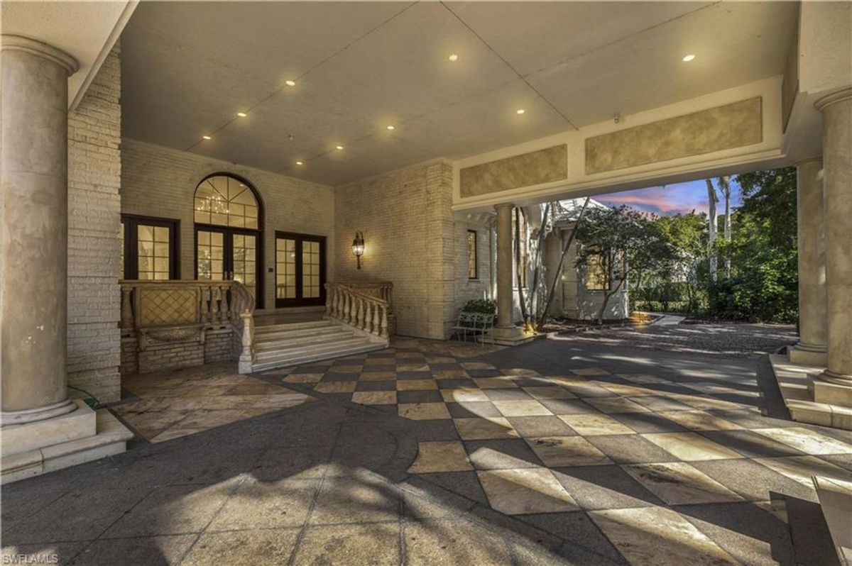 Grand covered entryway with elegant columns, arched glass doors, and a checkerboard-patterned floor welcomes guests in timeless style.