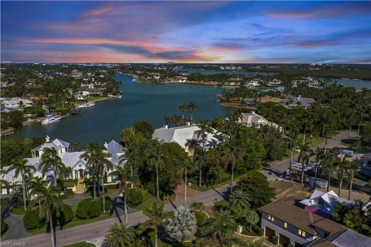 Aerial views showcase the serene waterfront neighborhood adorned with luxury homes, lush greenery, and tranquil canals under a colorful evening sky.