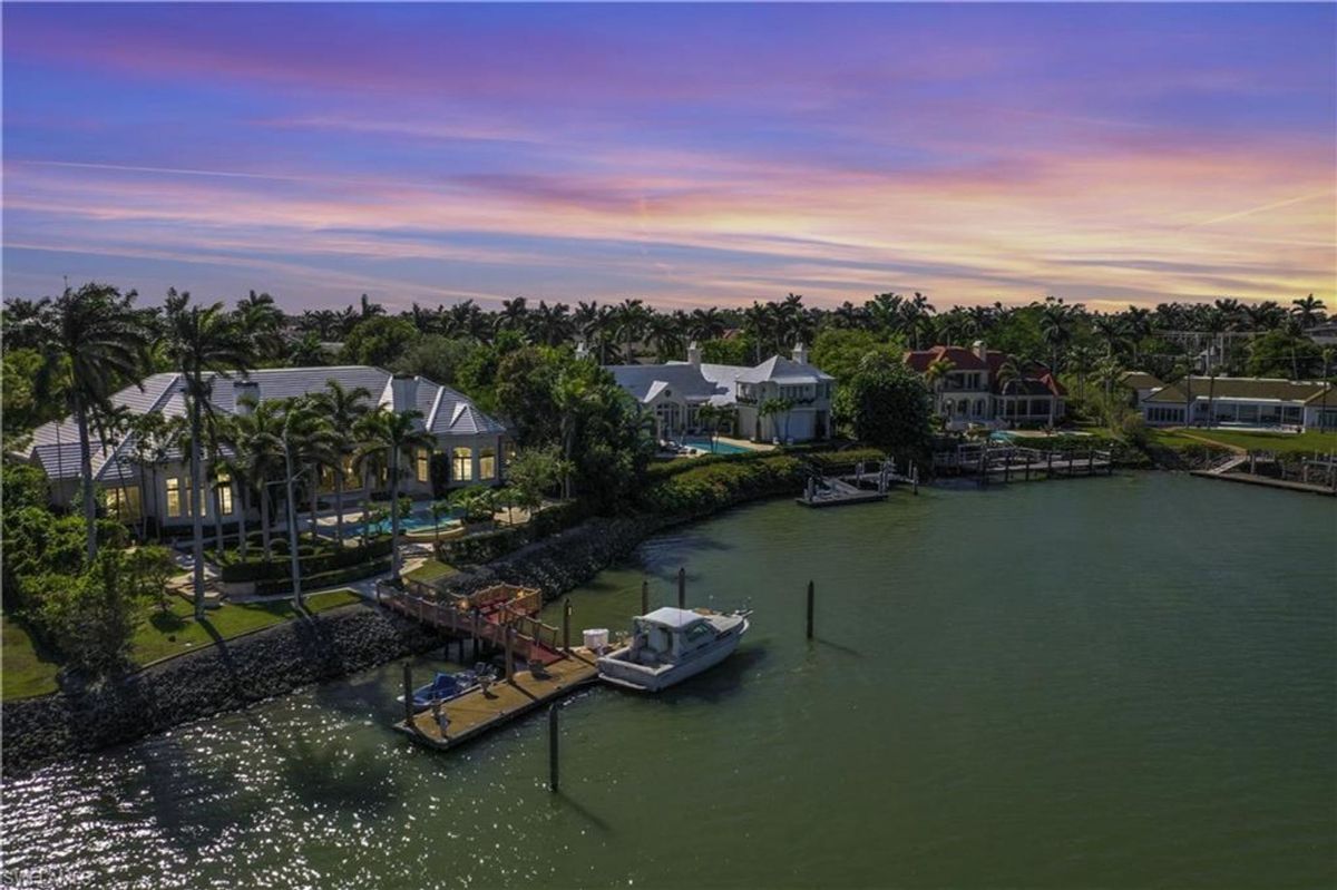 Waterfront luxury is showcased with this estate featuring a private dock, scenic views, and lush tropical landscaping under a stunning evening sky.