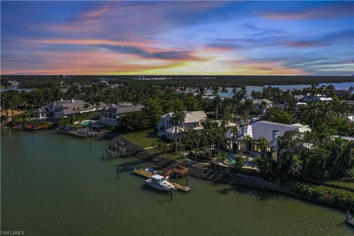 A peaceful waterfront enclave showcases luxurious homes, private docks, and lush tropical greenery under a dramatic sunset sky.