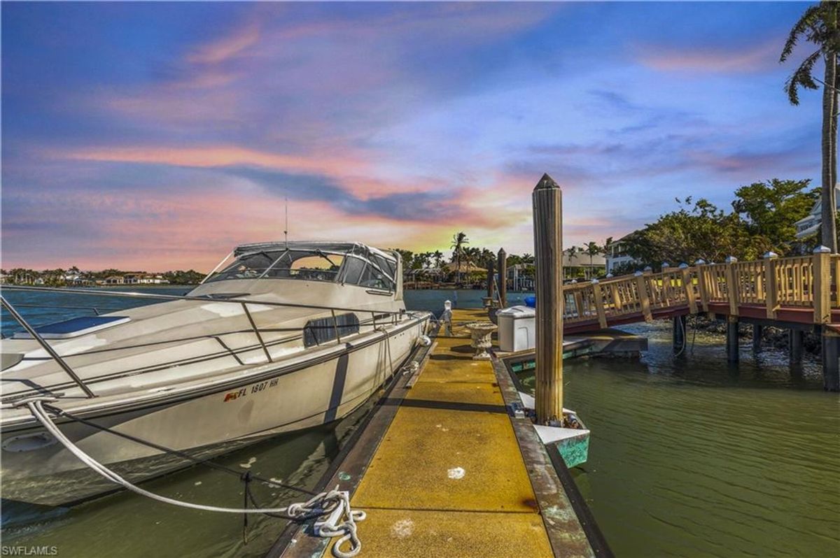 A private dock hosts a sleek yacht, framed by calm waters and a vibrant sunset, offering a serene waterfront retreat.