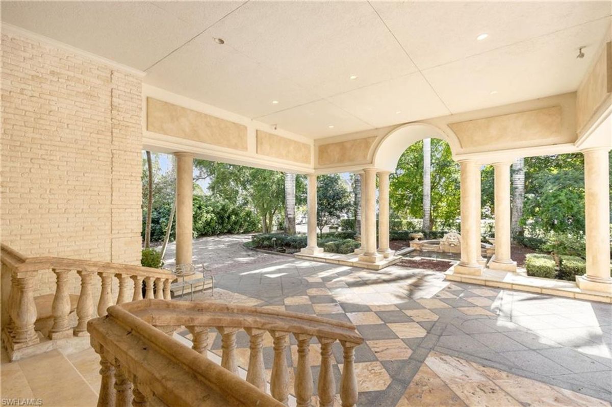 Open-air entryway features arched openings, stately columns, and intricate stone balustrades, blending classic design with natural surroundings.