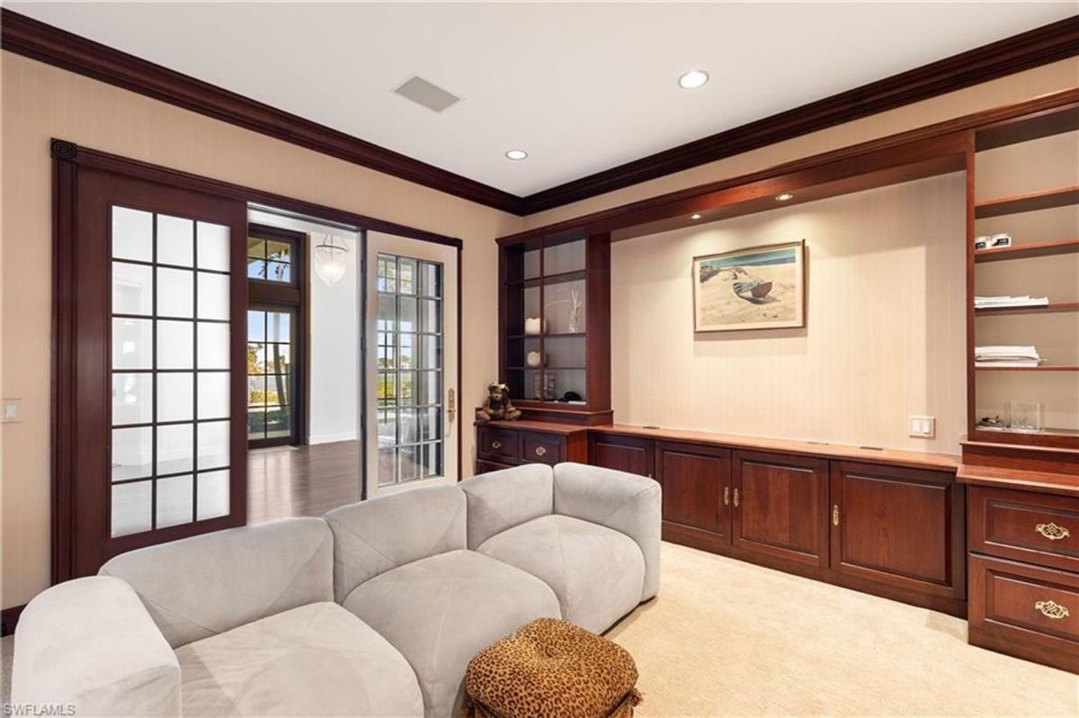 An intimate sitting room features rich wood cabinetry, built-in shelving, and frosted glass doors leading to a spacious living area.