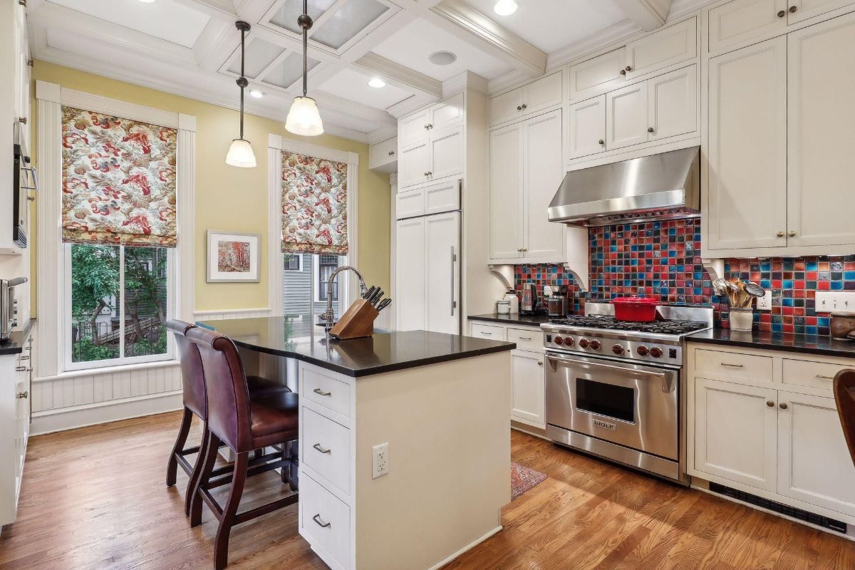 Kitchen with white cabinets, a large island, and colorful backsplash tile is shown.