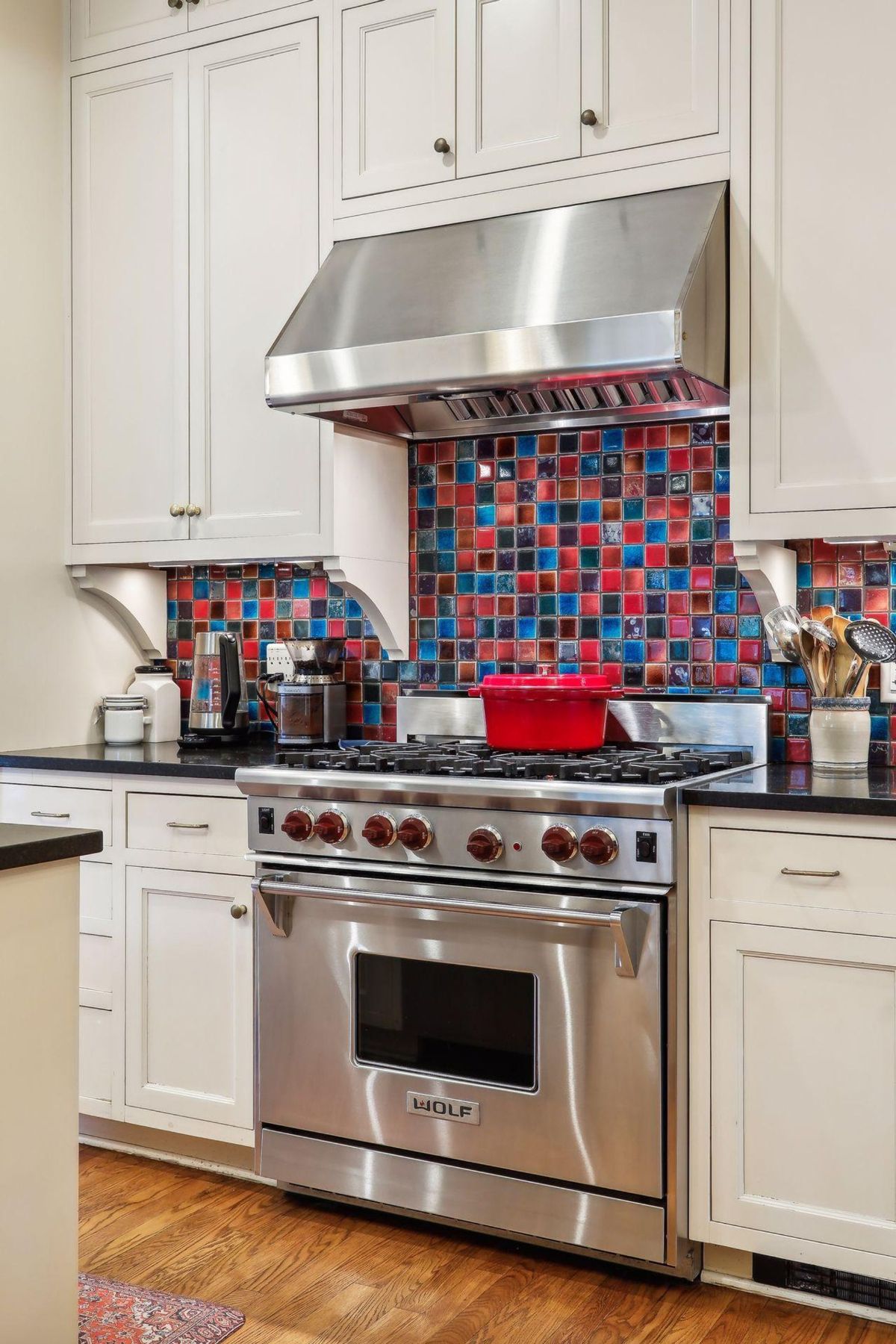 A stainless steel range and oven are the focal point of this kitchen, which features white cabinets and a colorful tile backsplash.