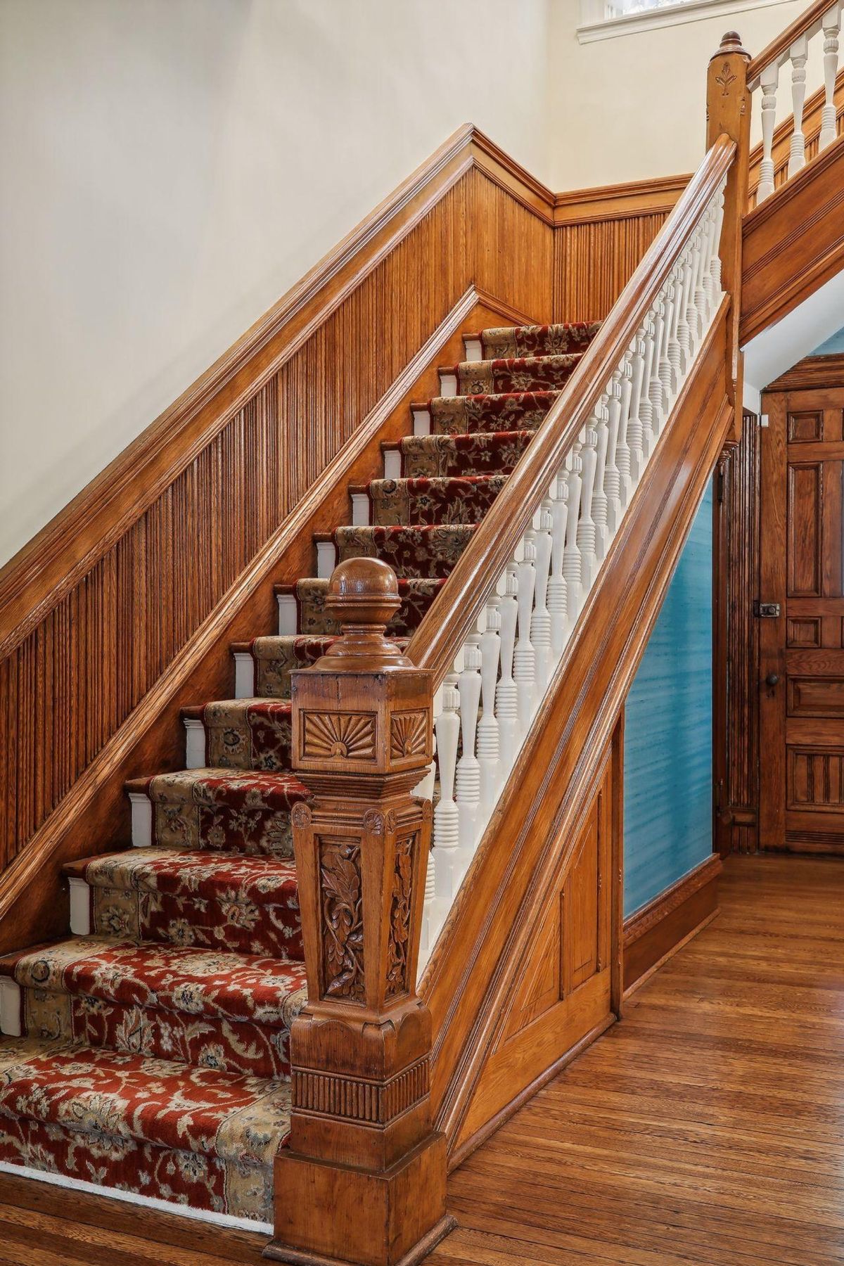 Grand staircase with ornate wooden banisters and a patterned runner is shown.