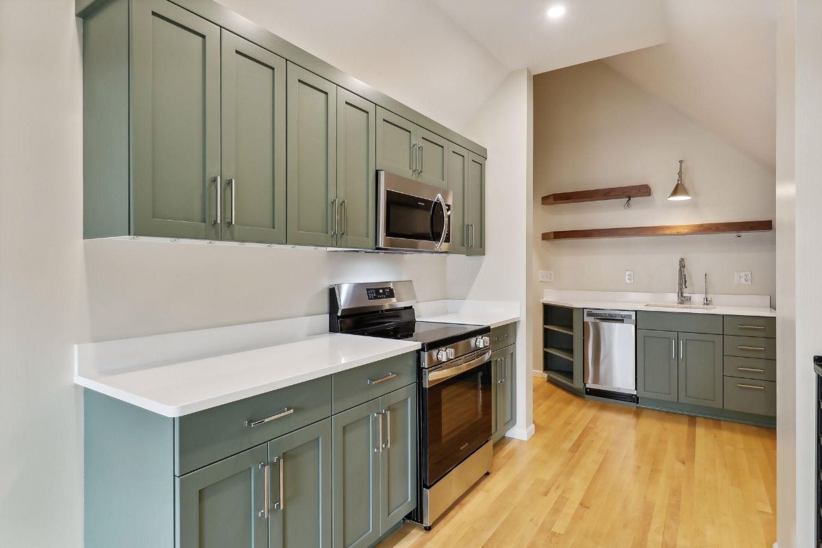 Kitchen with dark green cabinets and white countertops is shown.