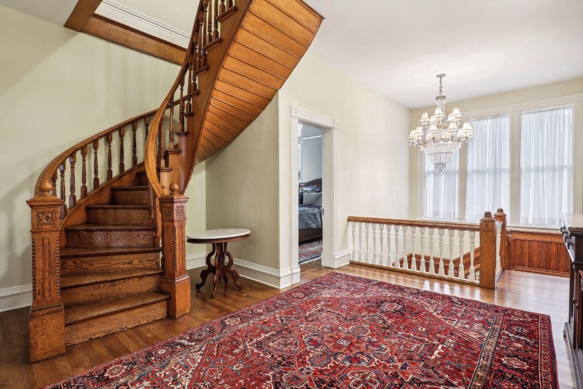 Curved wooden staircase dominates this image, which also features an ornate chandelier and an area rug.