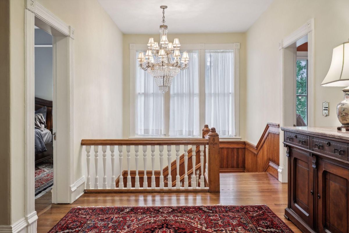 The hallway has wood floors and an area rug. A glimpse of a bedroom is visible through an open doorway.