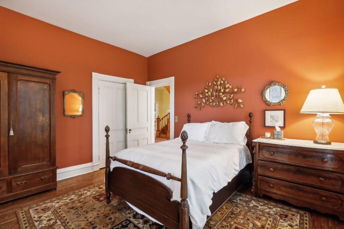 Bedroom features dark red walls, a wooden bed with white linens, and a dark wood dresser.