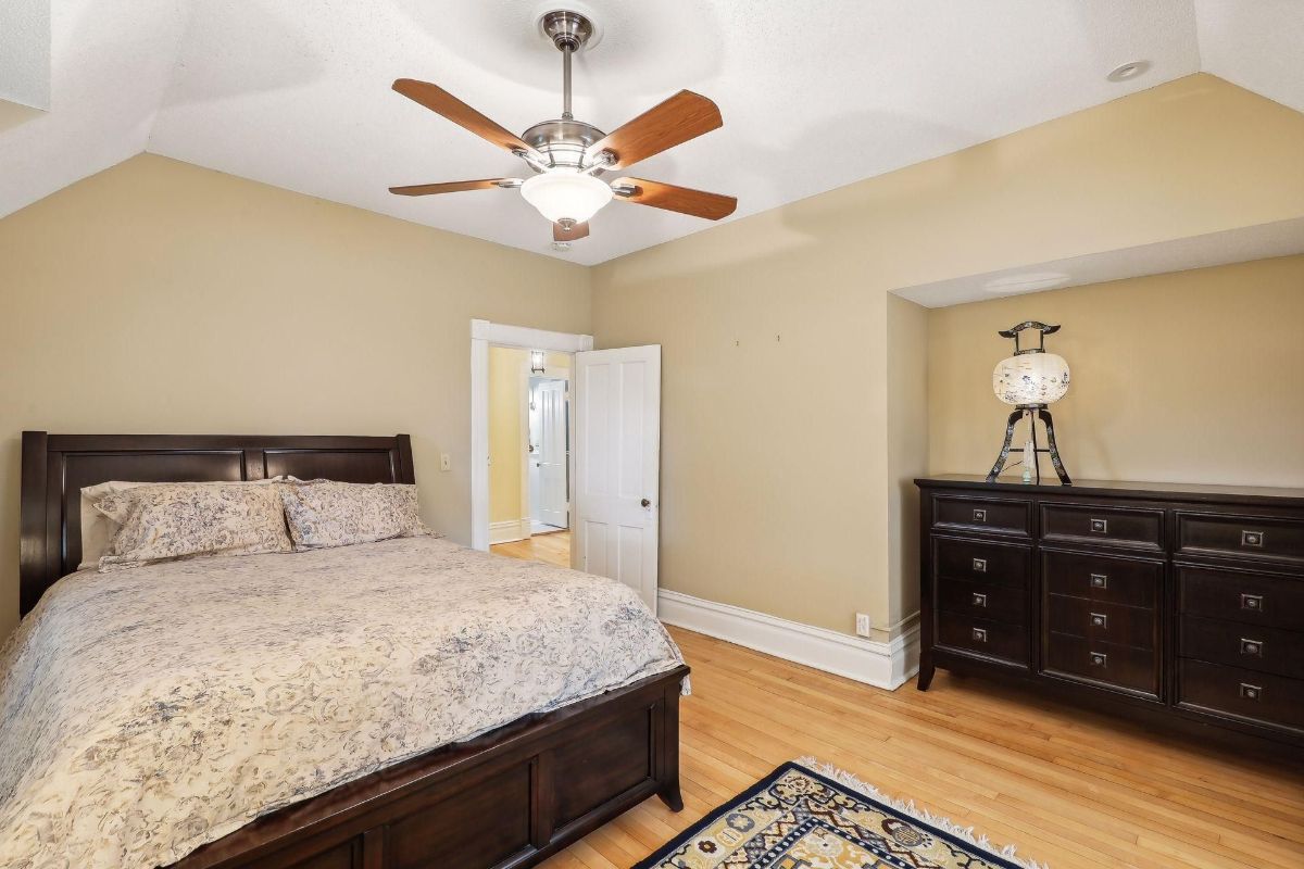 Bedroom with a ceiling fan, a large bed with a patterned comforter, and a dark dresser is shown.