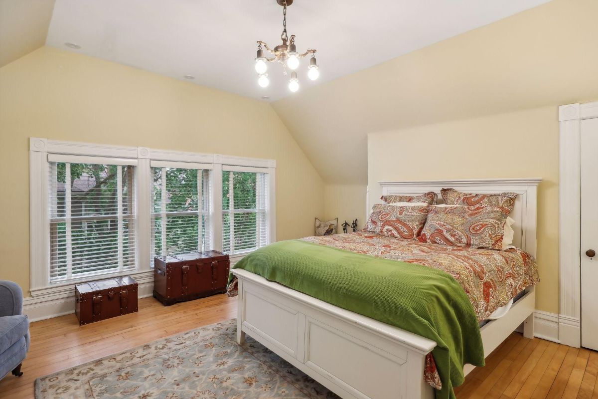 A bedroom with a white bed, patterned bedding, and dark brown chests.