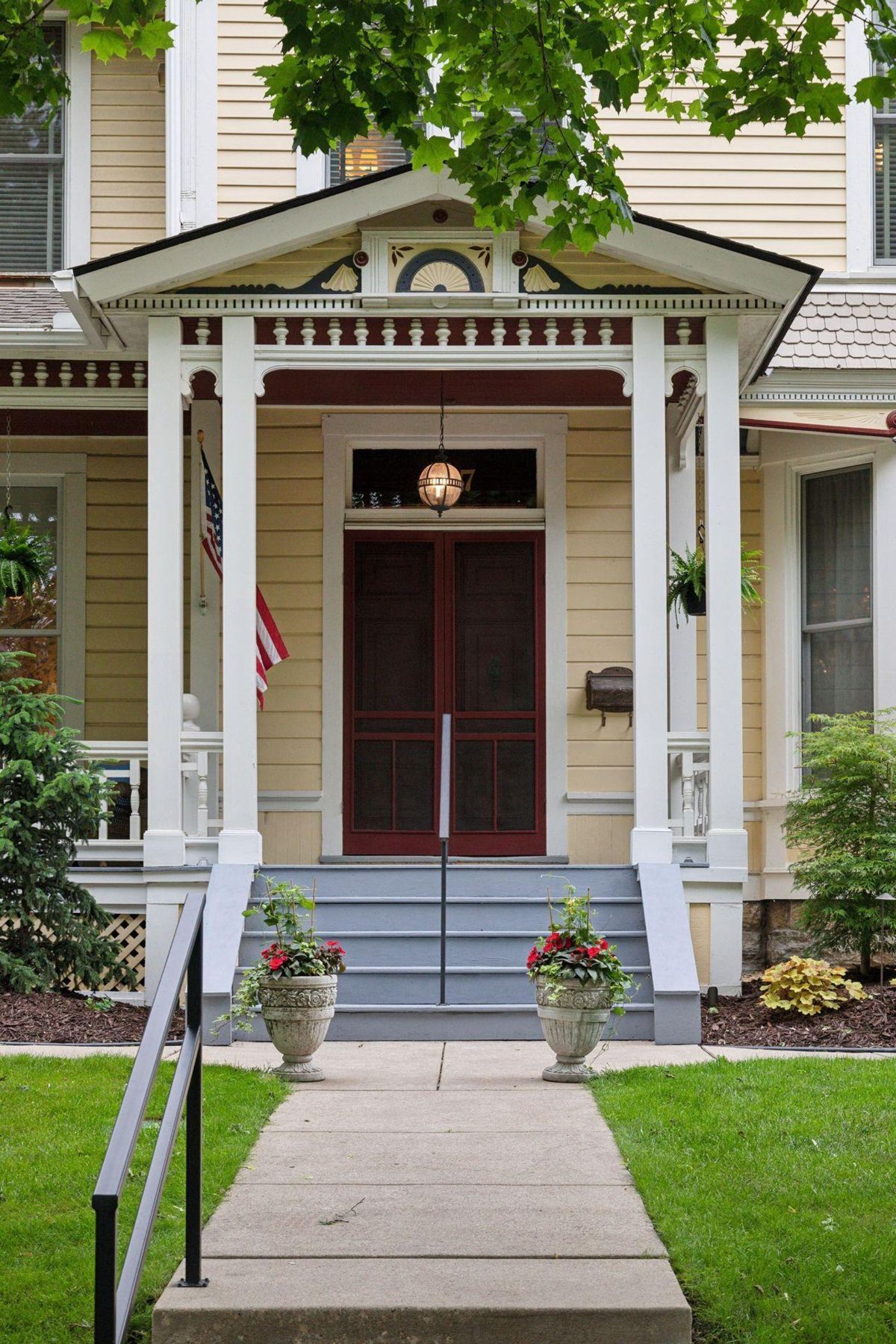 Ornate porch with double doors and planters graces the entrance of a light-yellow house.