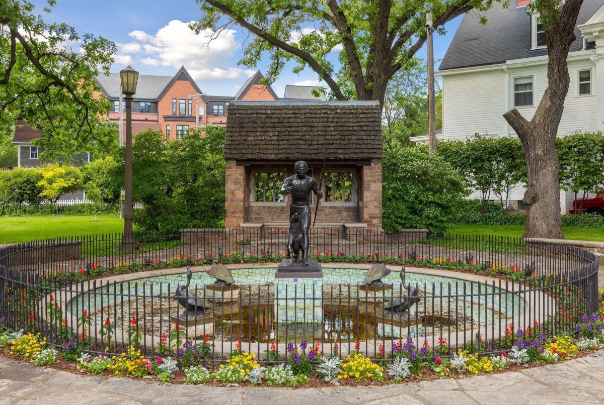 A statue in a circular fountain, surrounded by flowers and trees.