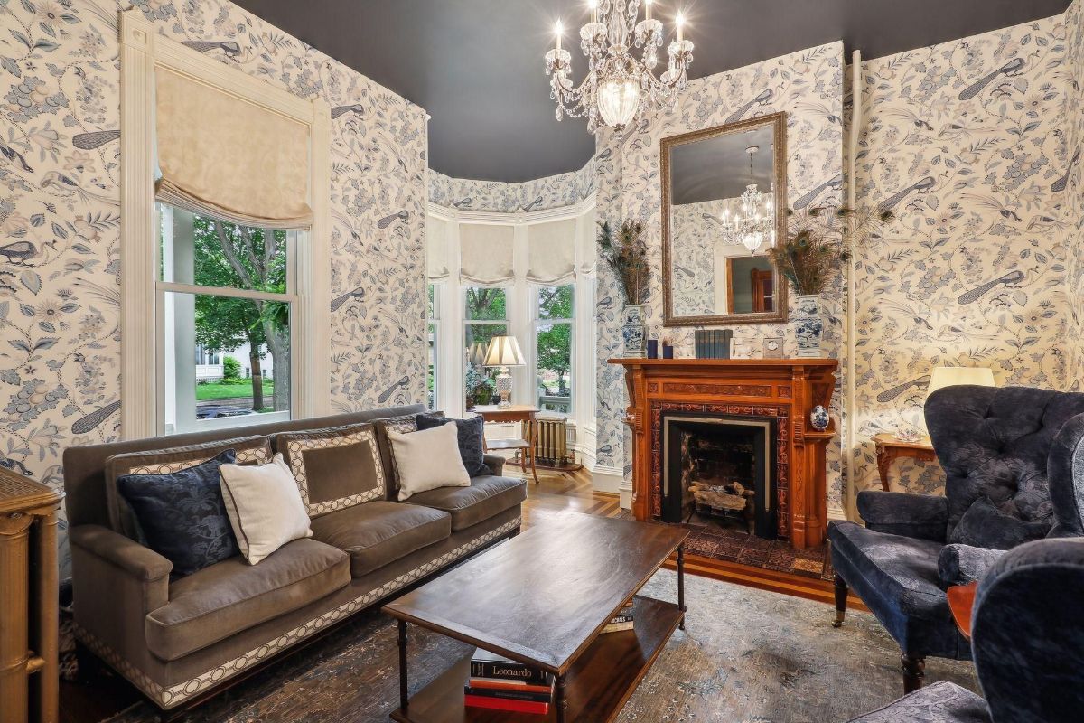 An elegant living room features a fireplace, patterned wallpaper, and a comfortable sofa.